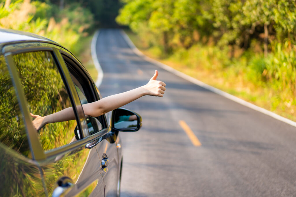 Woman in the car showing her thumb up sign. Safe driving concept. Transportation and driving concept and background. Road trip driving. Countryside. 